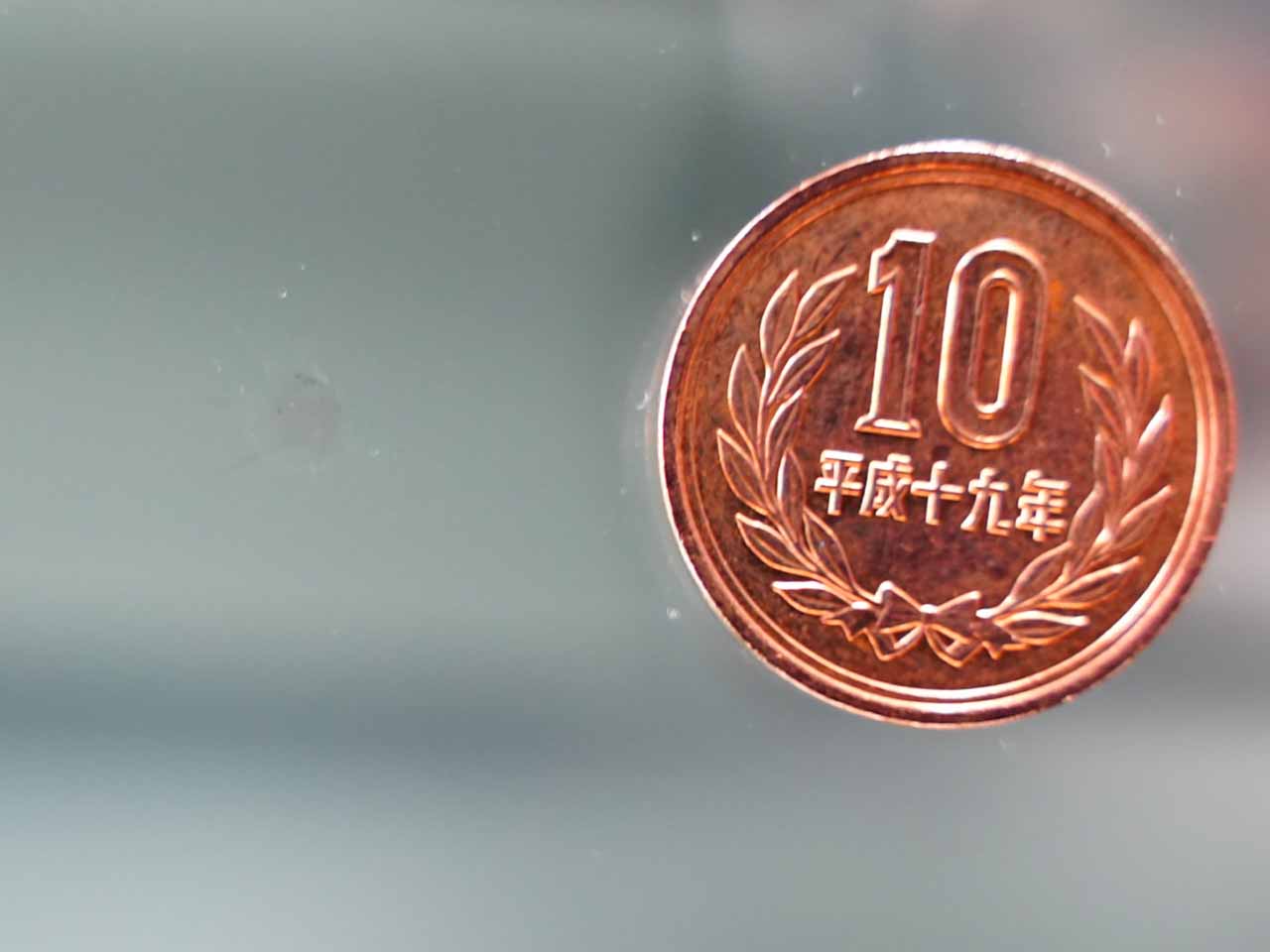 ガラスに付いたキズをほとんど見えないくらいに修繕されたキズと10円玉