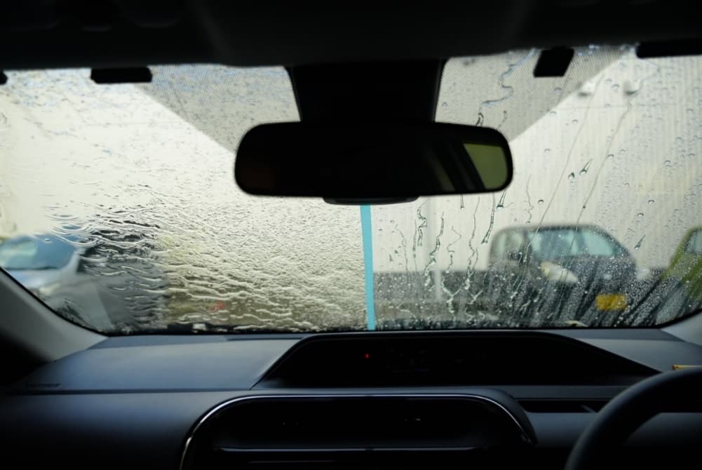 フロントガラスに半分だけコーティングをして比べている車の車内から見たガラス。左側:成功前 右側:施工後